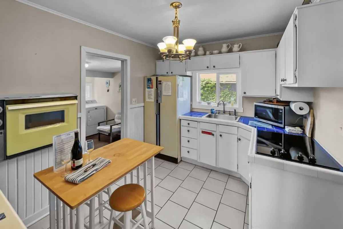 A cozy kitchen area with a cheerful yellow oven, wooden table, kitchen island, and a window offering natural light and a glimpse outside. The setup encourages family gatherings and casual dining, with elements like the kitchen island and table supporting group activities.