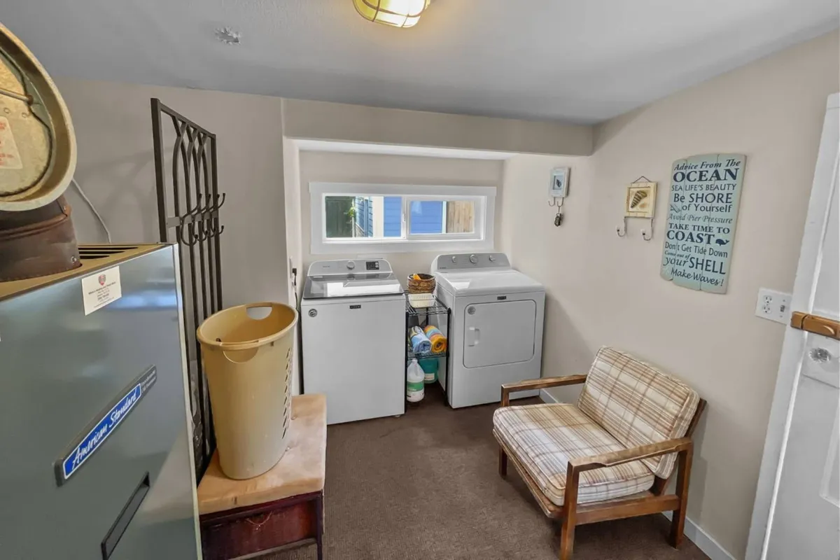 A practical yet cozy laundry area with washer and dryer, a comfortable chair, and bright natural light streaming through the window. The space feels welcoming and functional, ensuring convenience for families during their vacation stay.