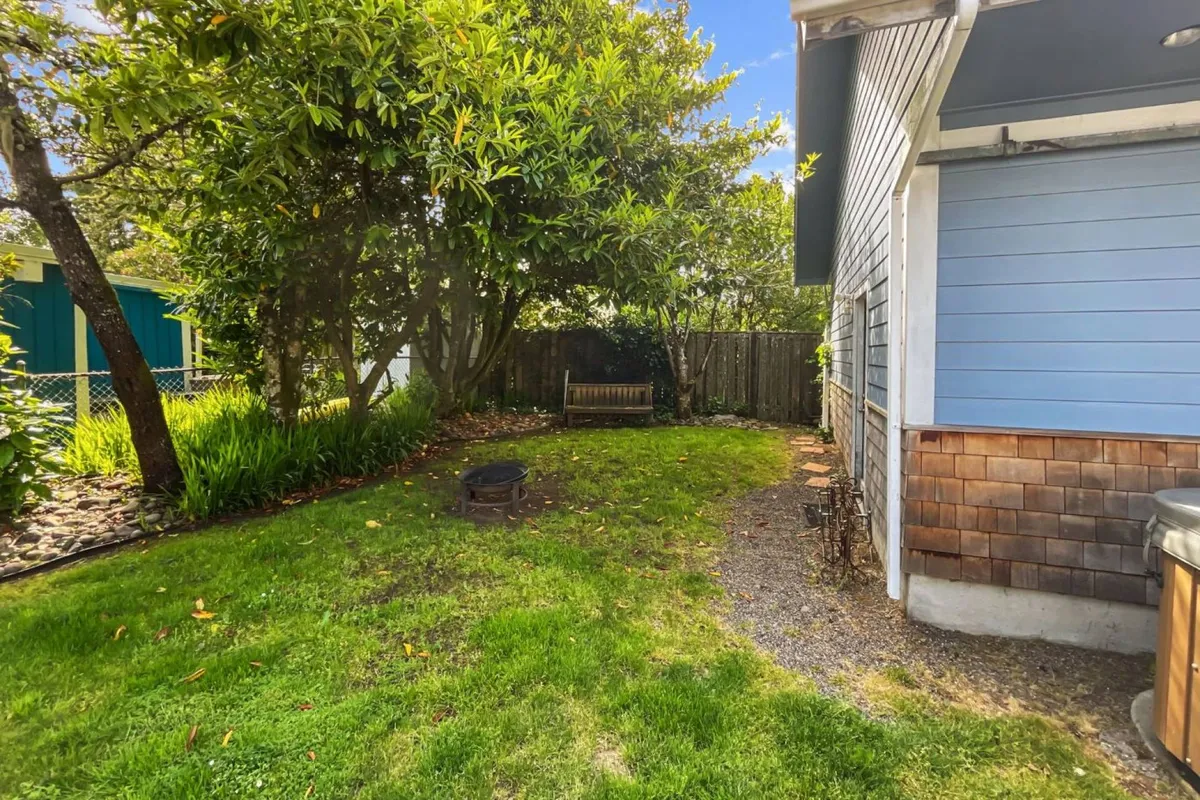 An inviting backyard scene featuring a bench and a fire pit, set among lush greenery. The fire pit is the focal point, surrounded by a natural setting that encourages gatherings, storytelling, or peaceful moments at dusk.