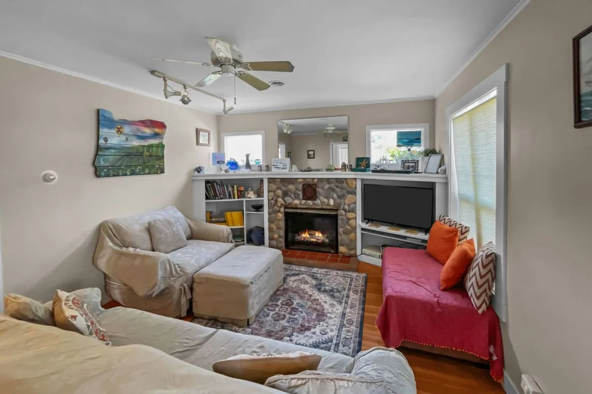 A warmly lit living room featuring an inviting seating area centered around a fireplace, surrounded by tasteful wall art and built-in bookshelves. The space exudes comfort and encourages intimate conversations, reading, or simply relaxing after a day at the beach.