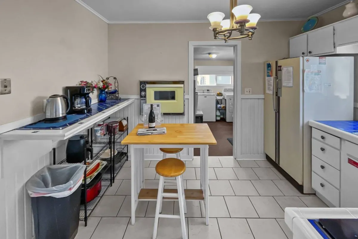 A view of a kitchen table surrounded by kitchen appliances and an open doorway, suggesting a seamless flow between spaces. The scene is set for casual family meals or stories shared over breakfast, with an inviting, lived-in feel.