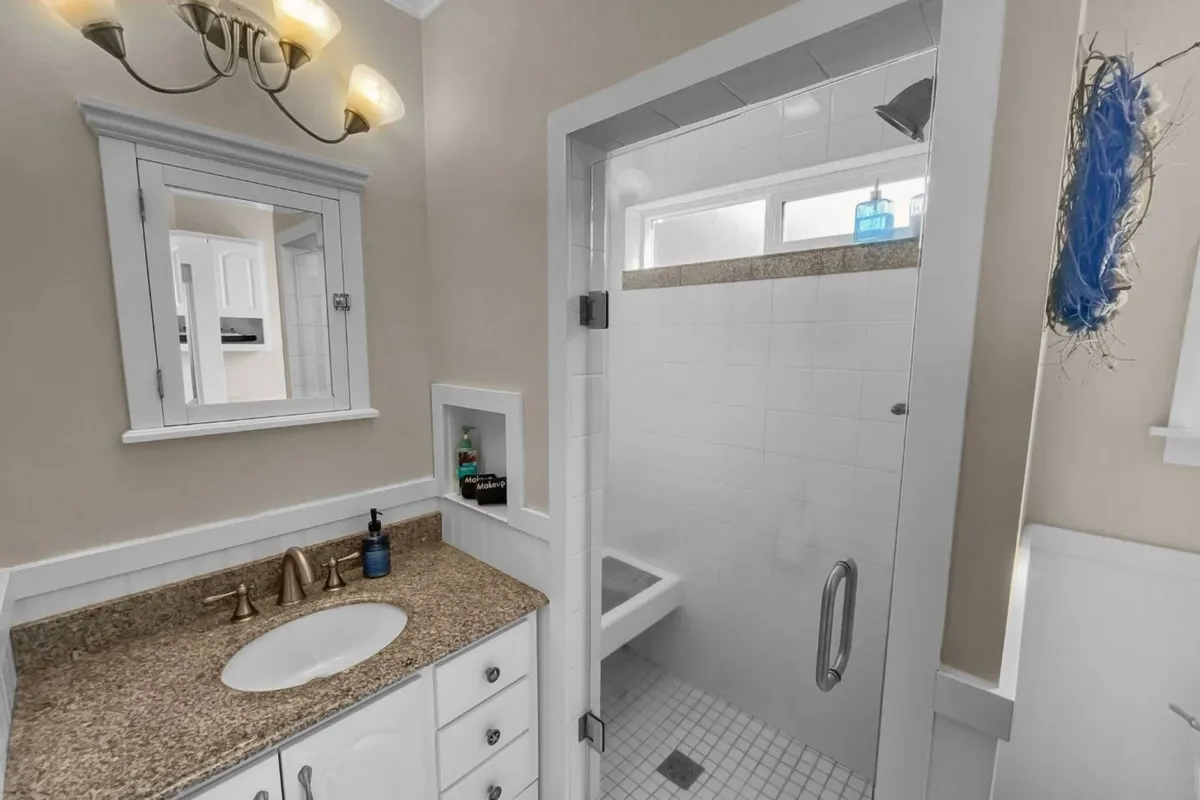 This inviting bathroom scene features a bright vanity with a mirror and a modern shower area, evoking a sense of calm and serenity. The space is softly lit, reflecting the gentle ambiance of a seaside retreat and suggesting a peaceful place to start or end the day.